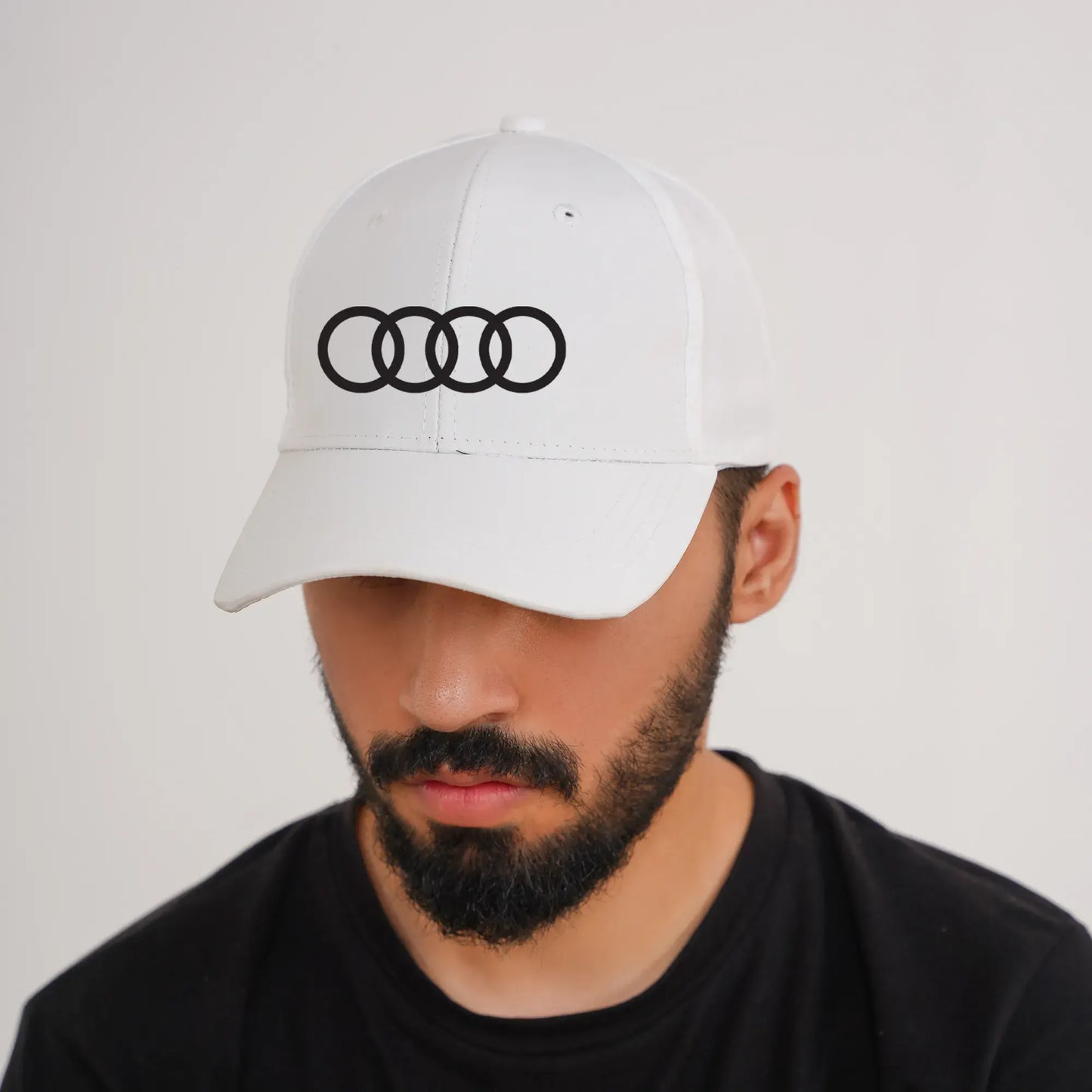 Man wearing a white cap with an Audi logo on a plain background