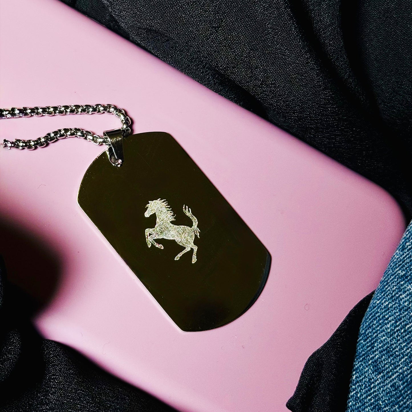 Black dog tag with a horse emblem on a pink surface