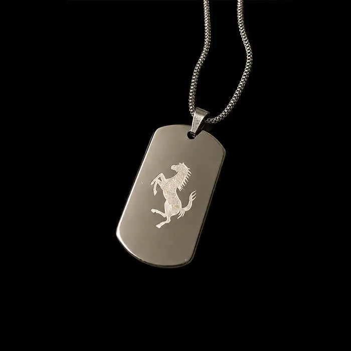 A silver-tone metal dog tag pendant featuring an engraved Ferrari prancing horse logo, suspended from a matching silver chain against a solid black background.