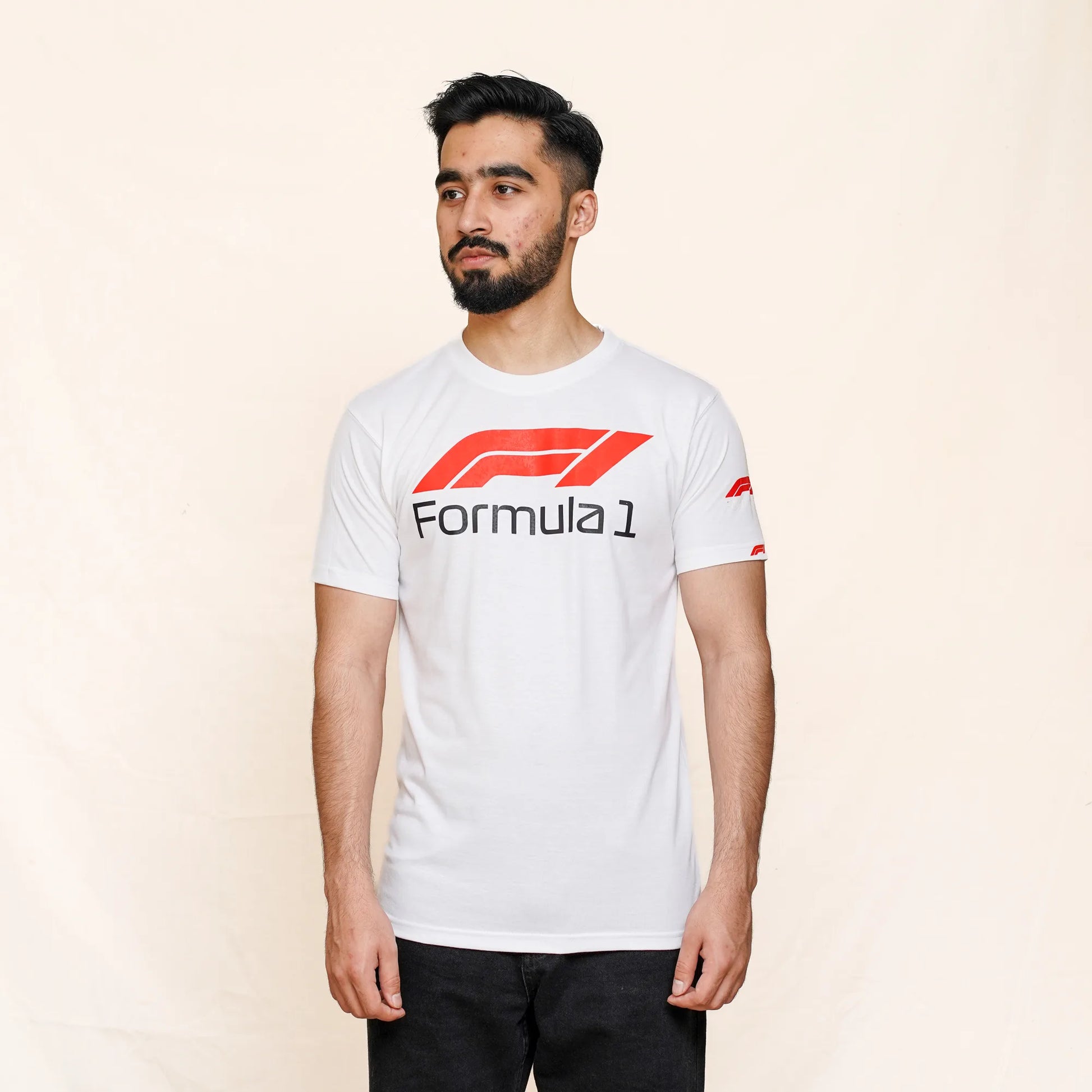 A man wearing a white round neck t-shirt with the Formula 1 logo printed in the center, in a studio setting.