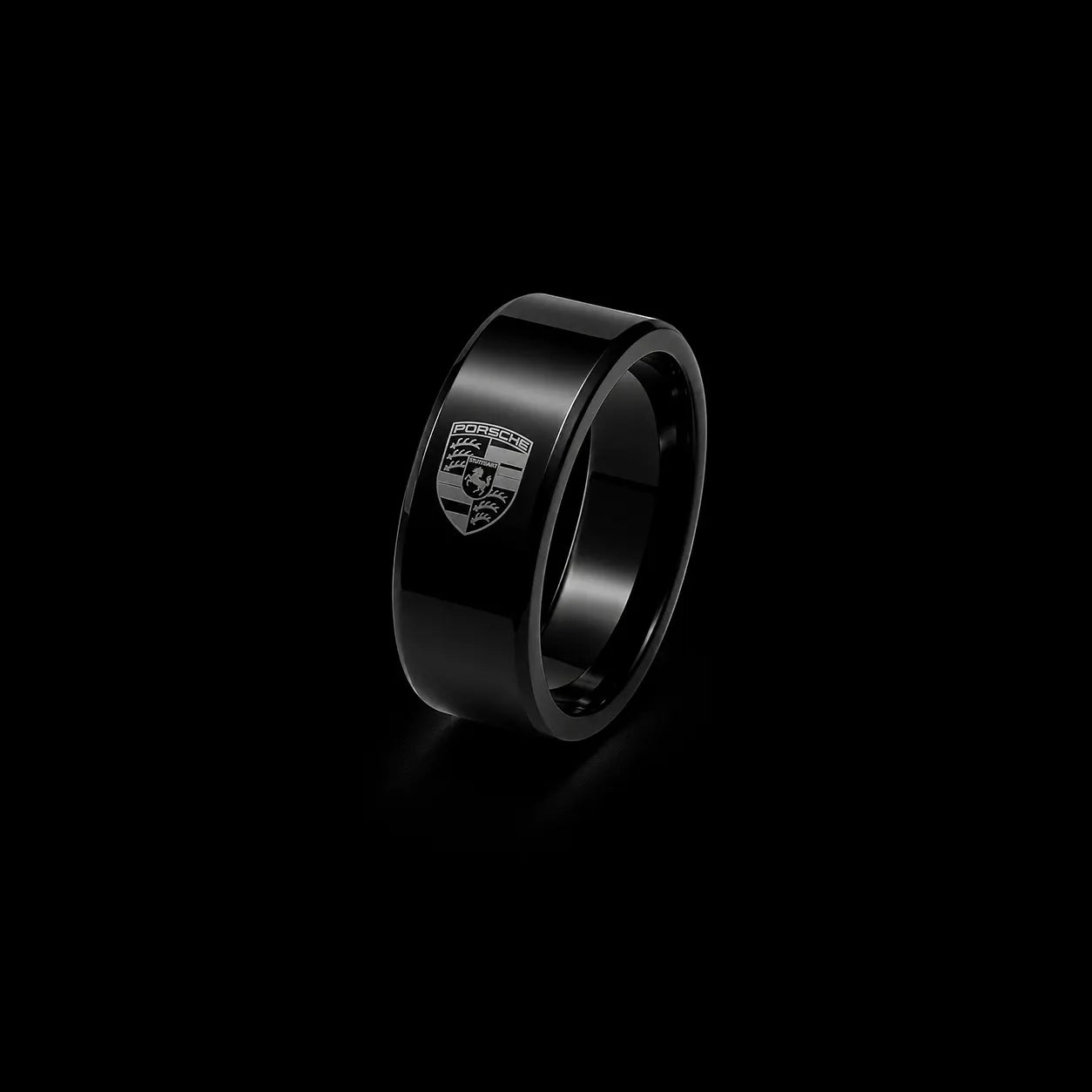 A black metallic ring featuring an engraved Porsche crest on its outer surface, set against a solid black background.
