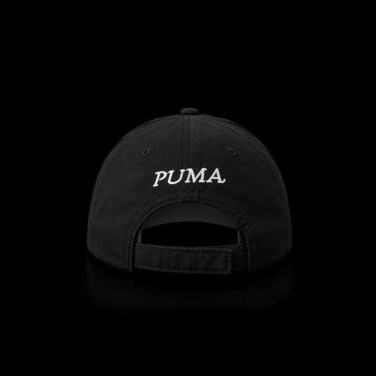 A black baseball cap shown from the back, featuring the word 'PUMA' embroidered in white script across the center. The cap is photographed against a solid black background with a subtle reflection below.