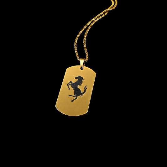 A gold-tone dog tag necklace featuring the black Ferrari prancing horse logo, suspended from a gold chain against a solid black background.