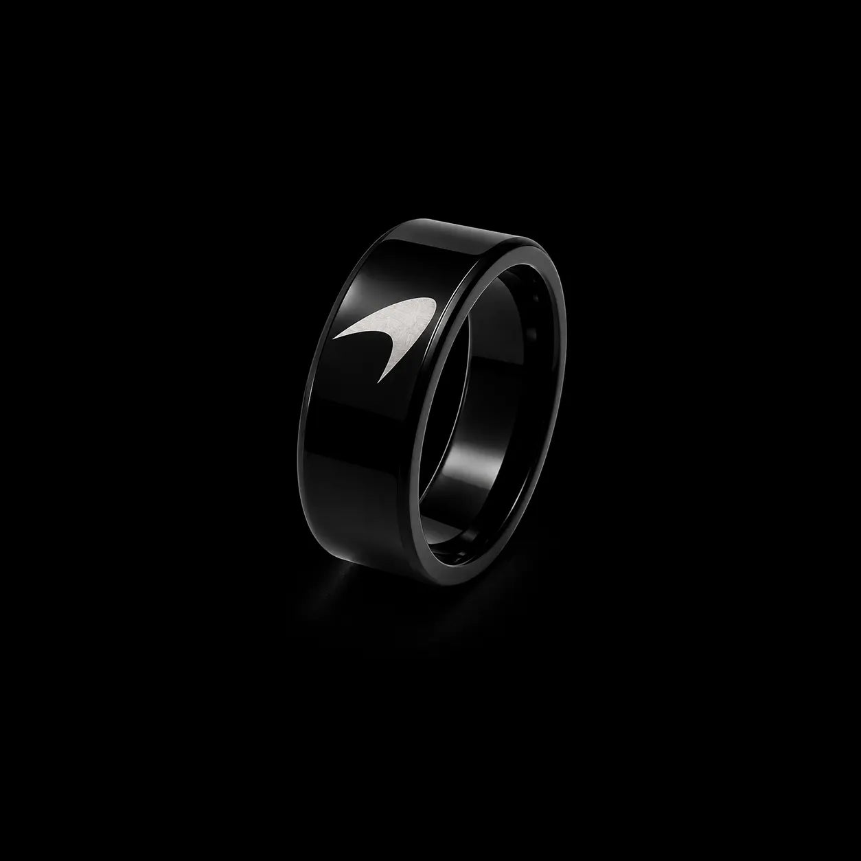 A glossy black ring with a polished silver chevron or wing-like inlay on the front, set against a solid black background.
