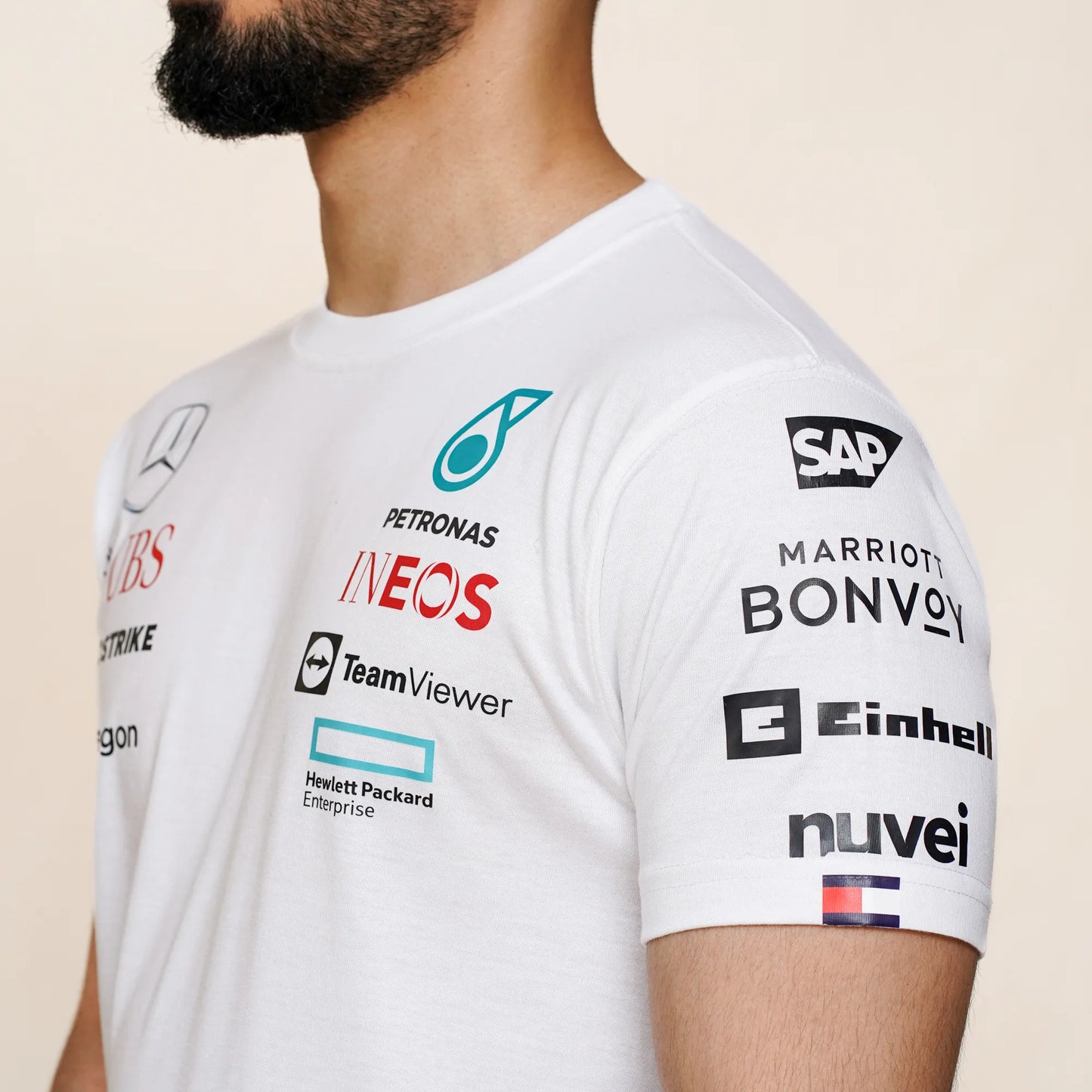 Motorsport theme white tee with printed sponsor icons displayed on a person standing against neutral background.